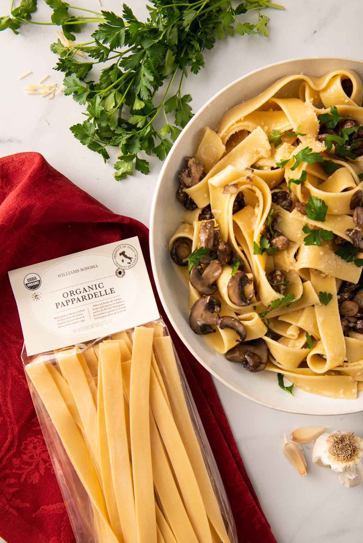 Williams Sonoma's organic pappardelle pasta next to a bowl of cooked creamy mushroom pasta.