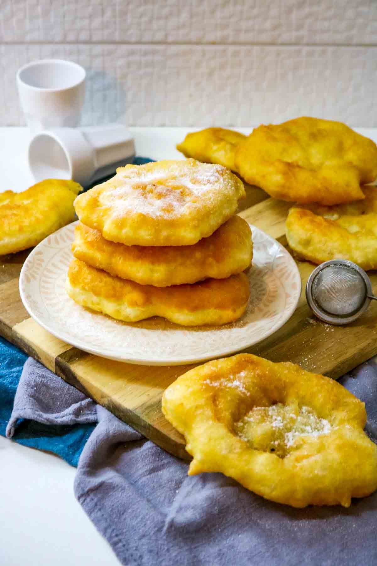 Mekitsi on a white plate surrounded by other pieces of sugared fried dough.