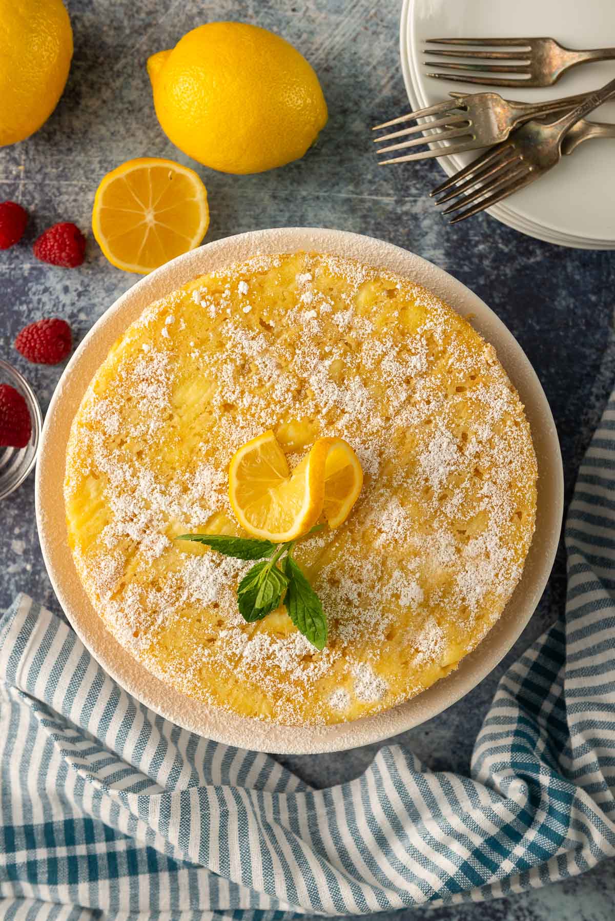 A top down photo of an Italian lemon ricotta cake decorated with a twisted lemon slice and powdered sugar.