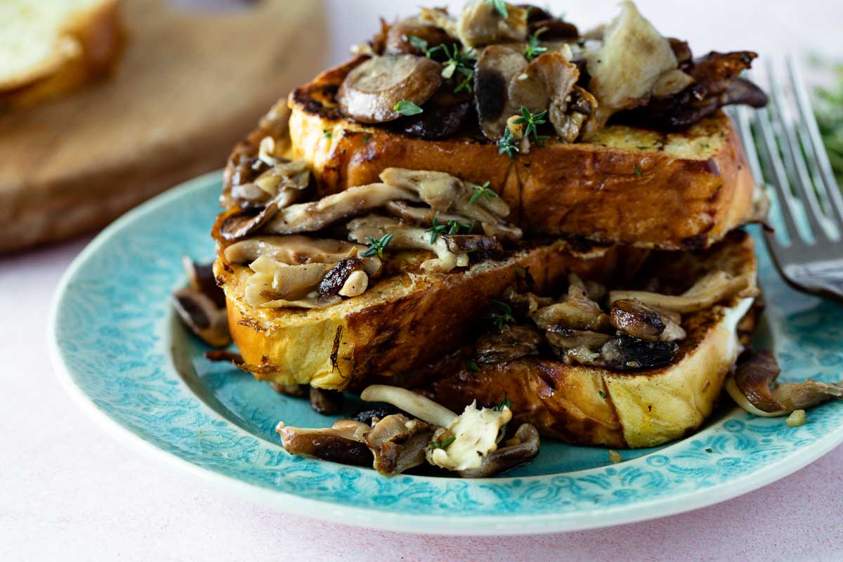 3 slices of savory french toast with garlicky mushrooms and thyme on a blue plate.