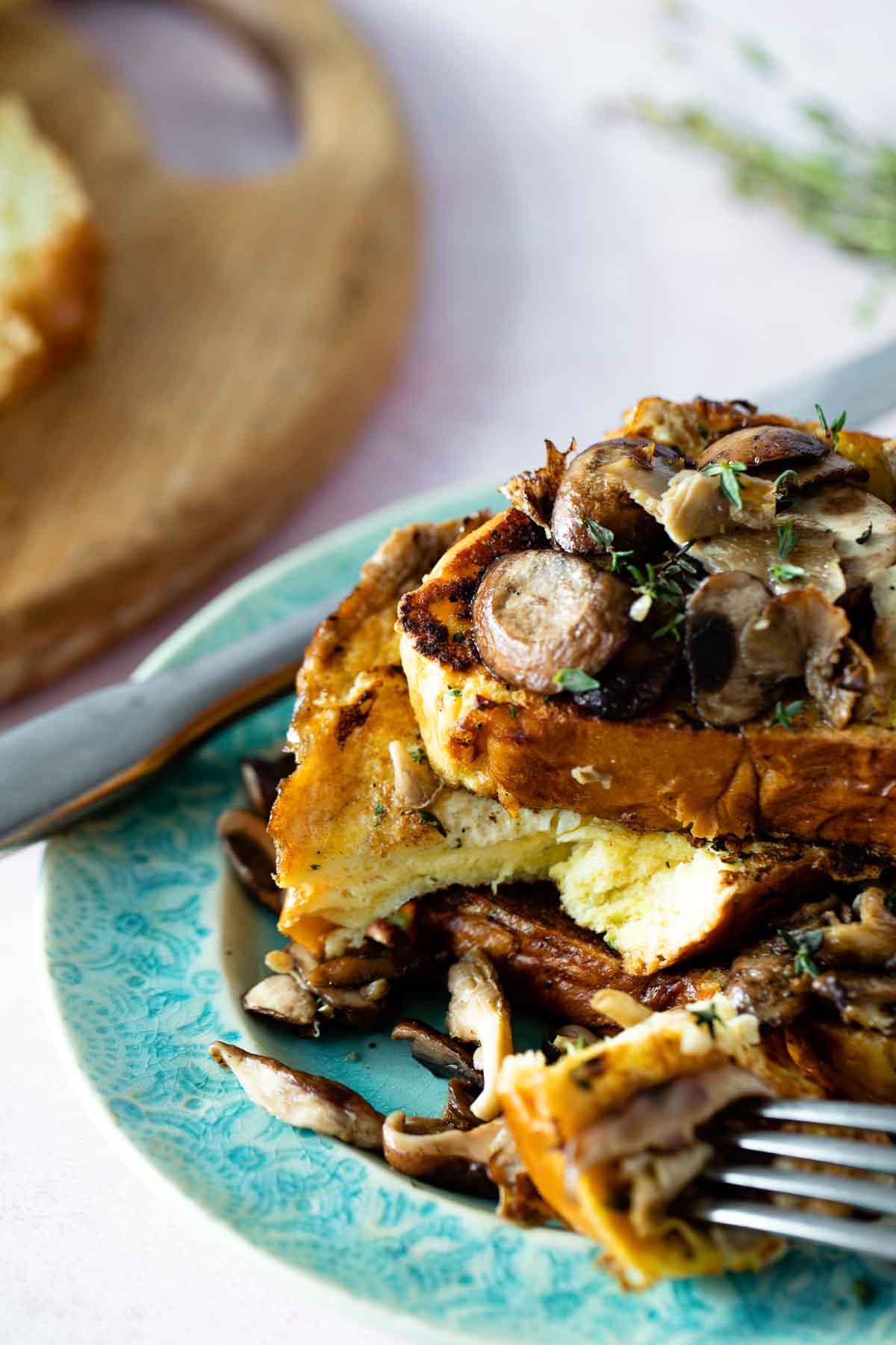 A stack of savory french toast with garlicky mushrooms and thyme. A bite is missing.