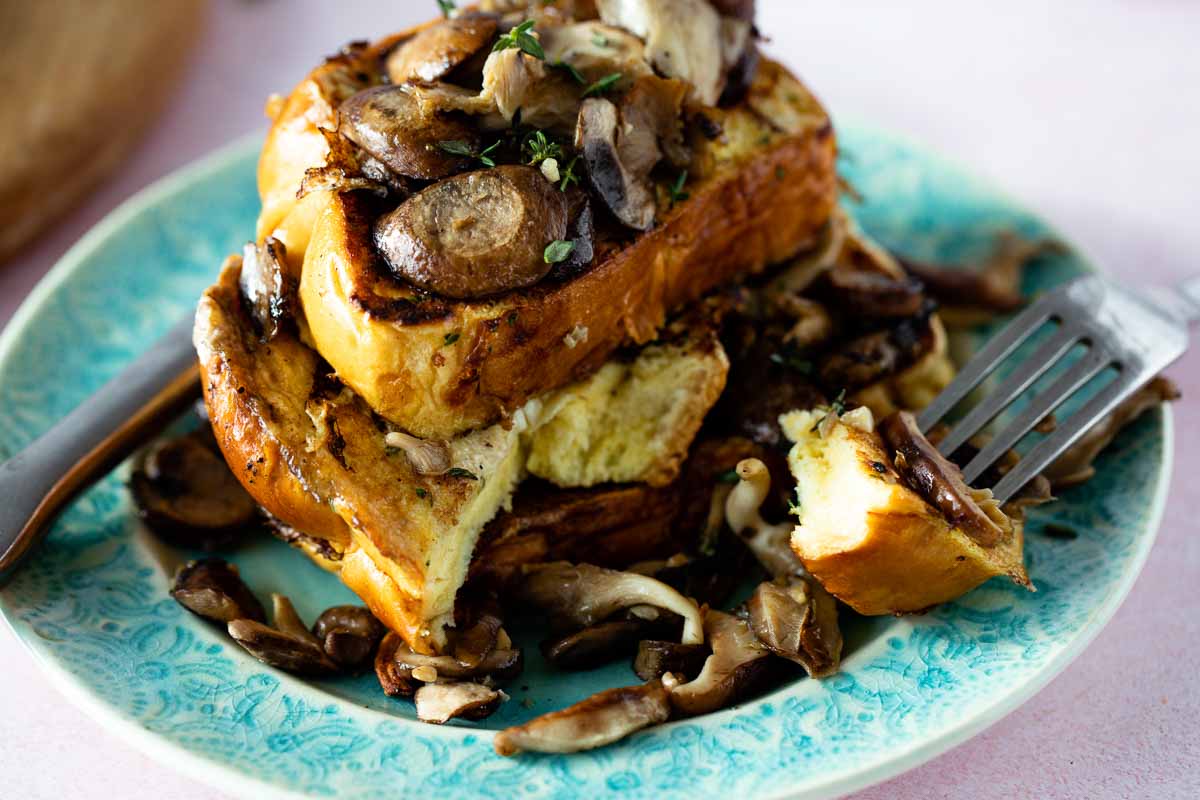 A fork stealing away a bite of french toast with mushrooms.