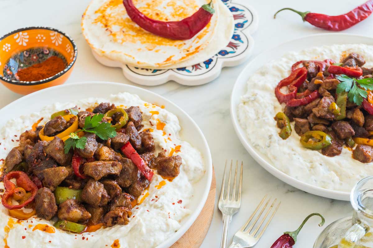 Two plates of Alinazik next to each other with some chilis around them.