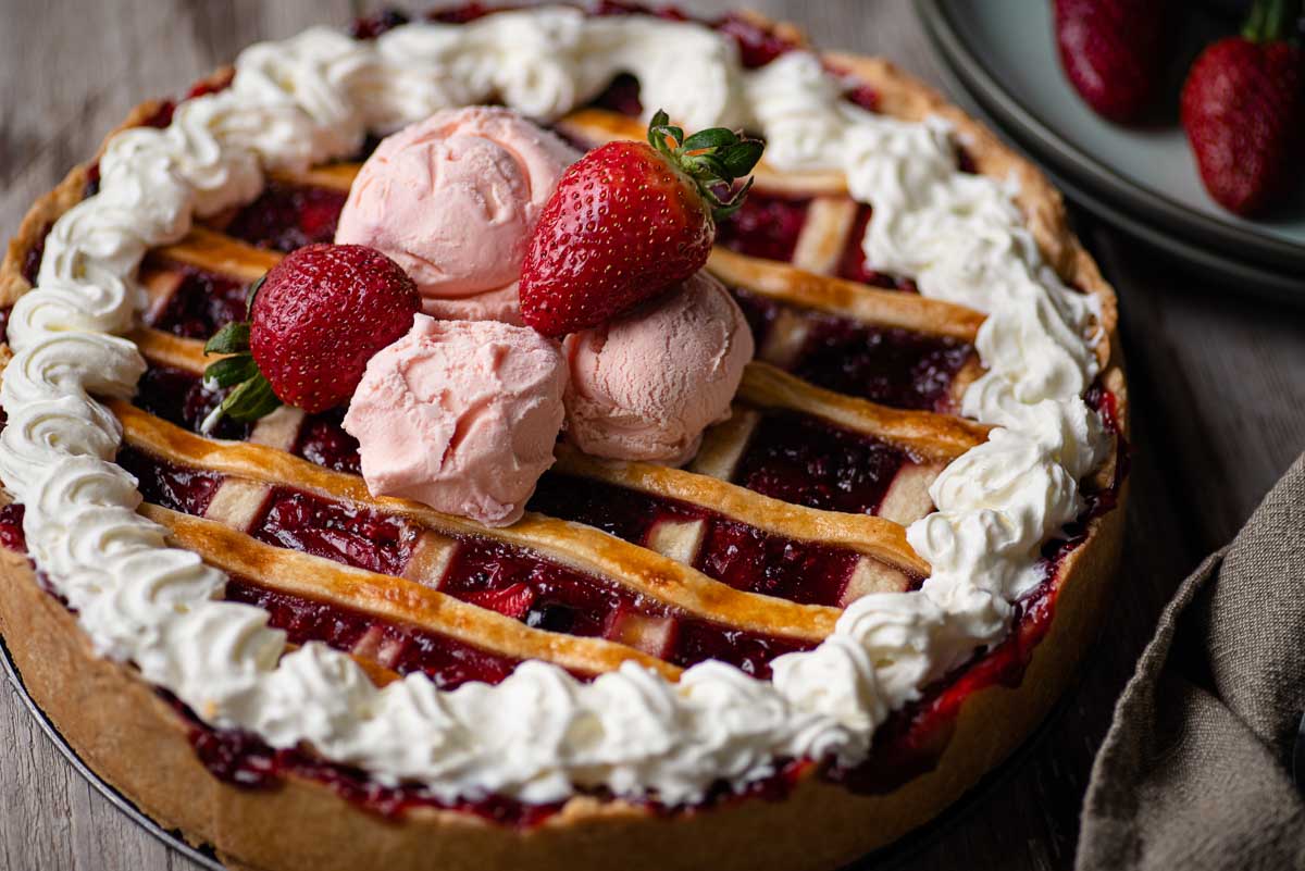 A strawberry pie, made using the recipe from the game Celeste. The pie is latticed, and topped with a whipped cream border, three scoops of strawberry ice cream, and two strawberries.