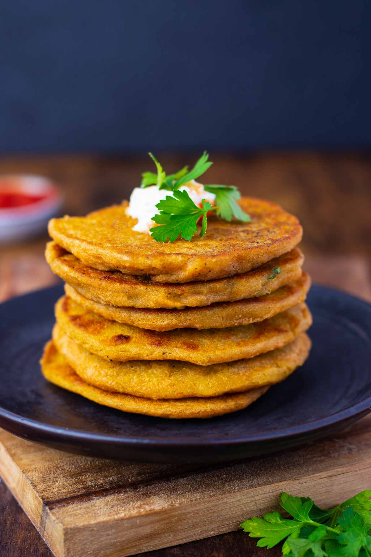 Six lentil pancakes stacked on a blue plate. The pancakes are garnished with a butter butter and cilantro.