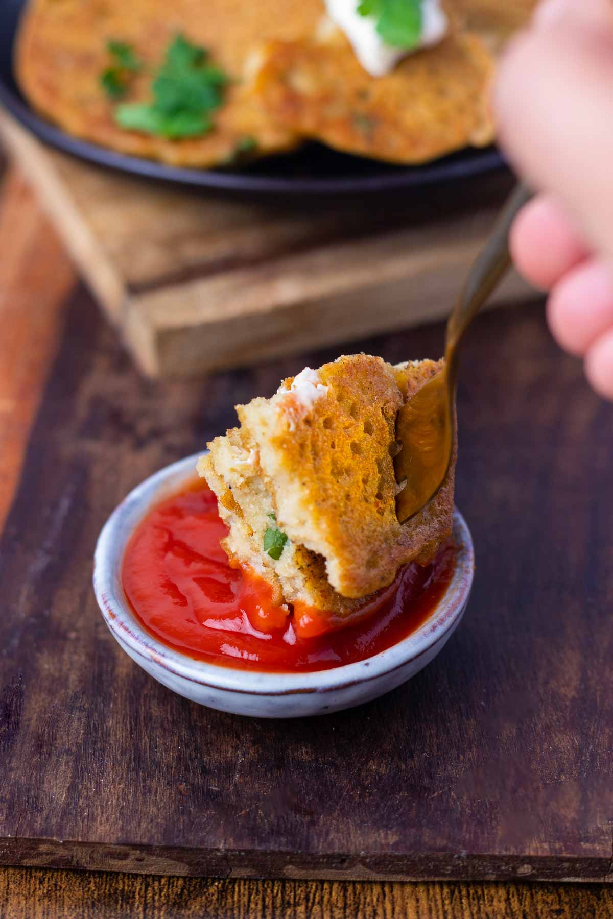 A forkful of lentil pancake being dipped into a small pot of tomato sauce.
