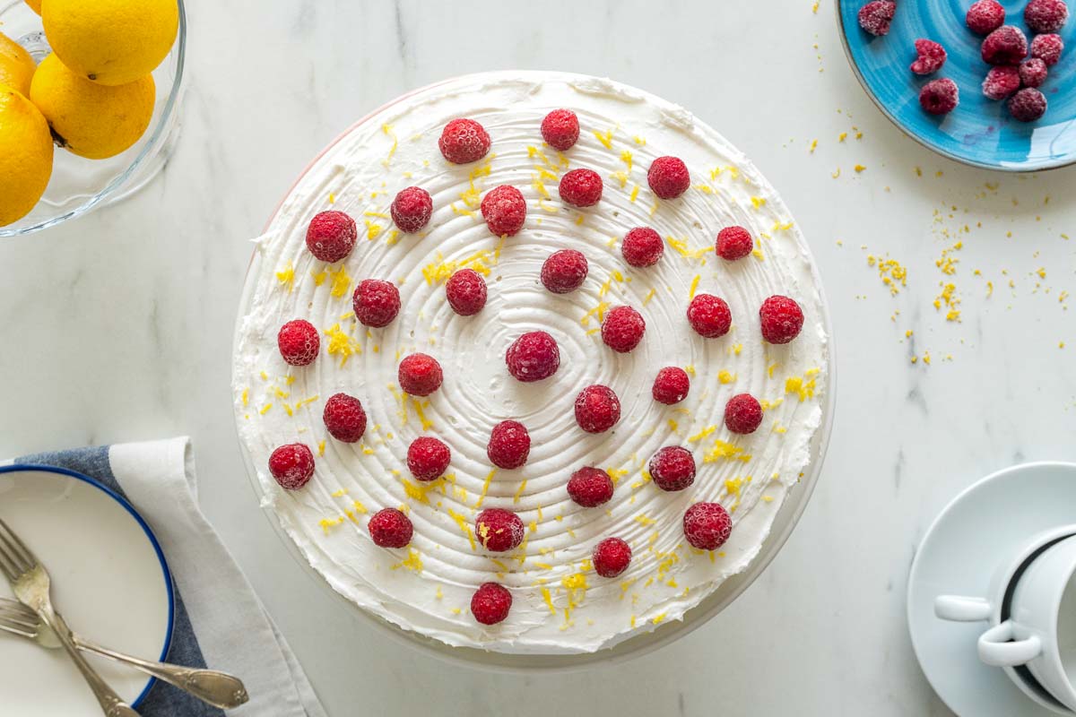 A lemon curd cake decorated with white chocolate Swiss buttercream, and raspberries.