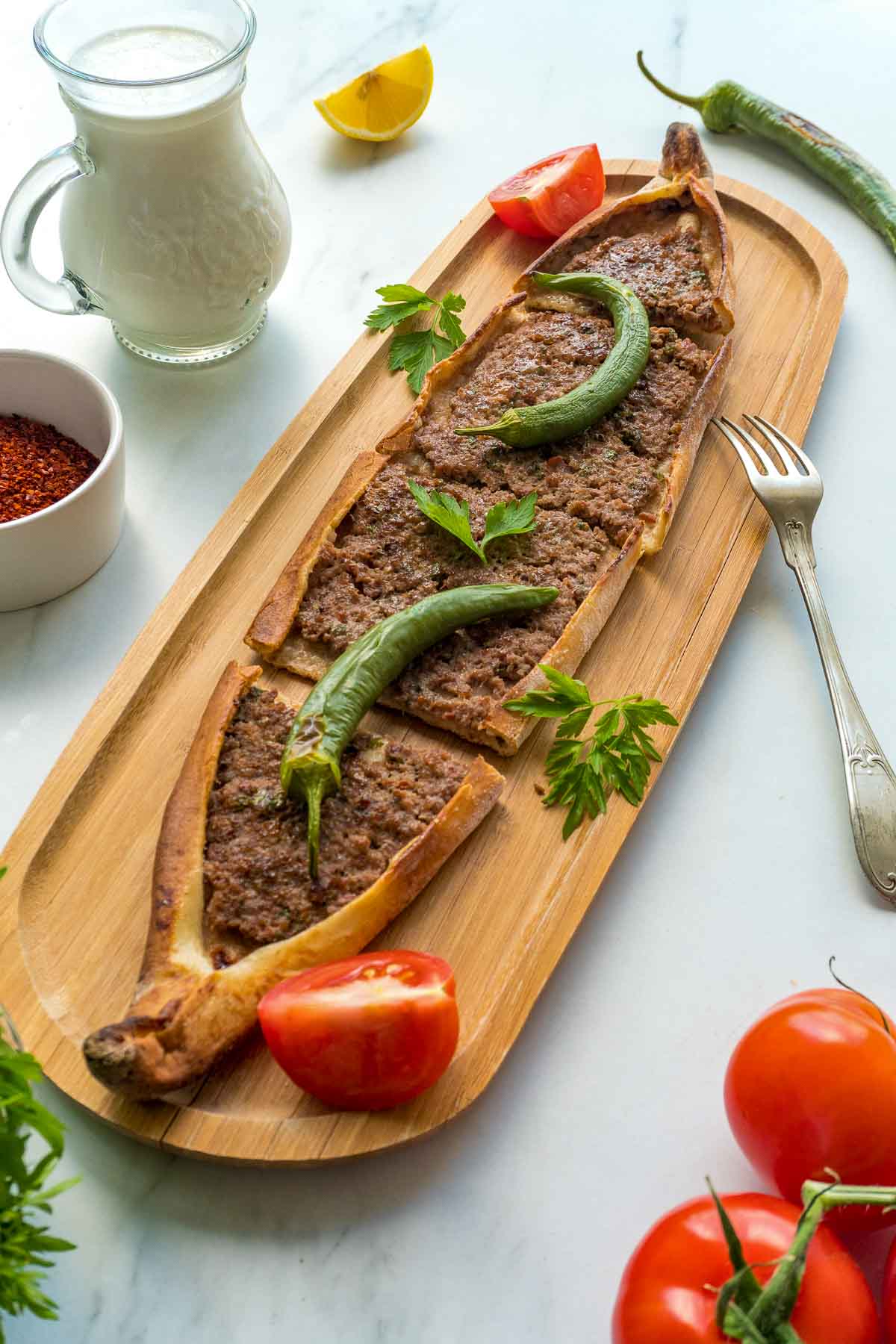 Turkish pide with ground beef on a wooden board with green chilis on top.