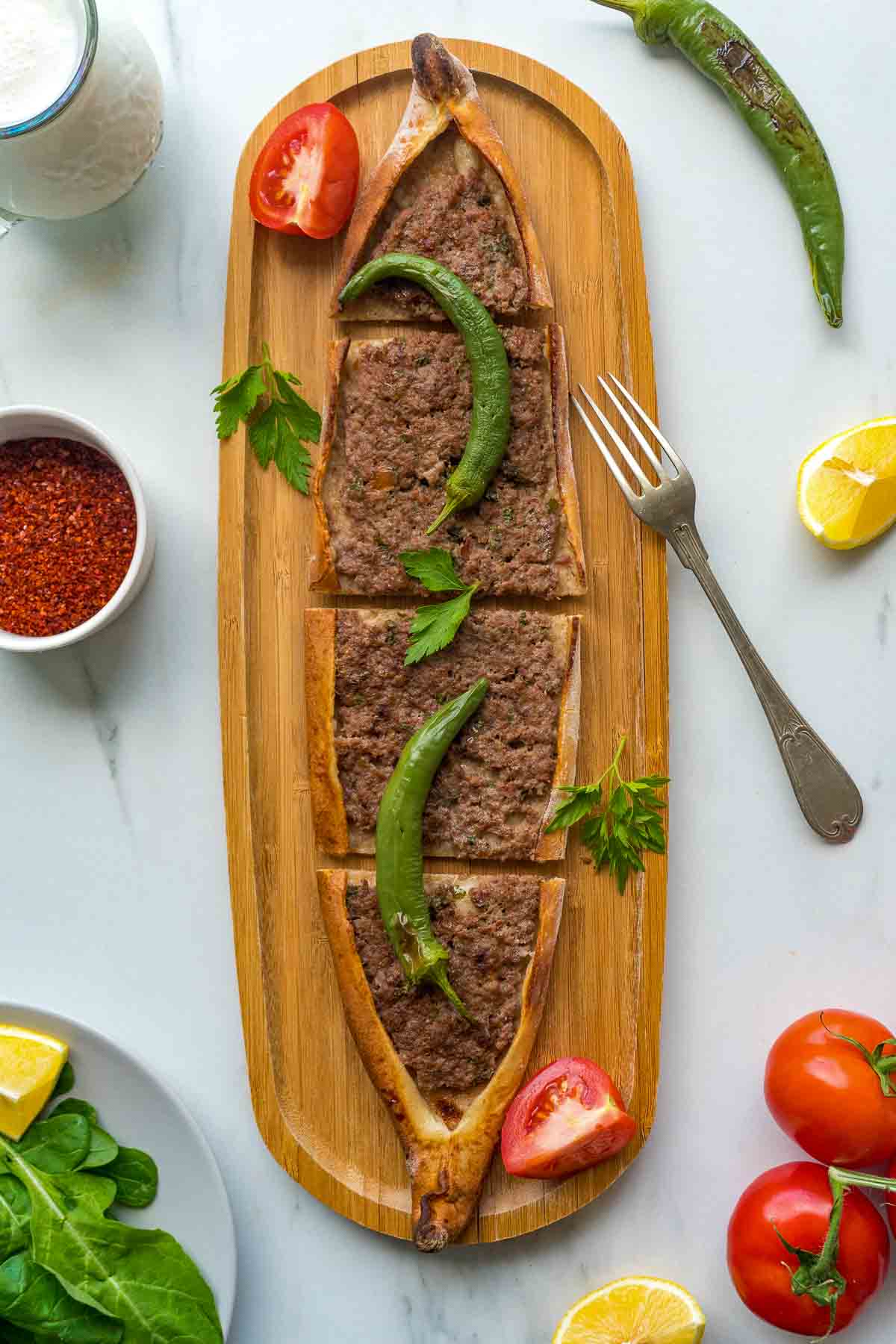 A flatlay with pide with ground meat on a wooden board.