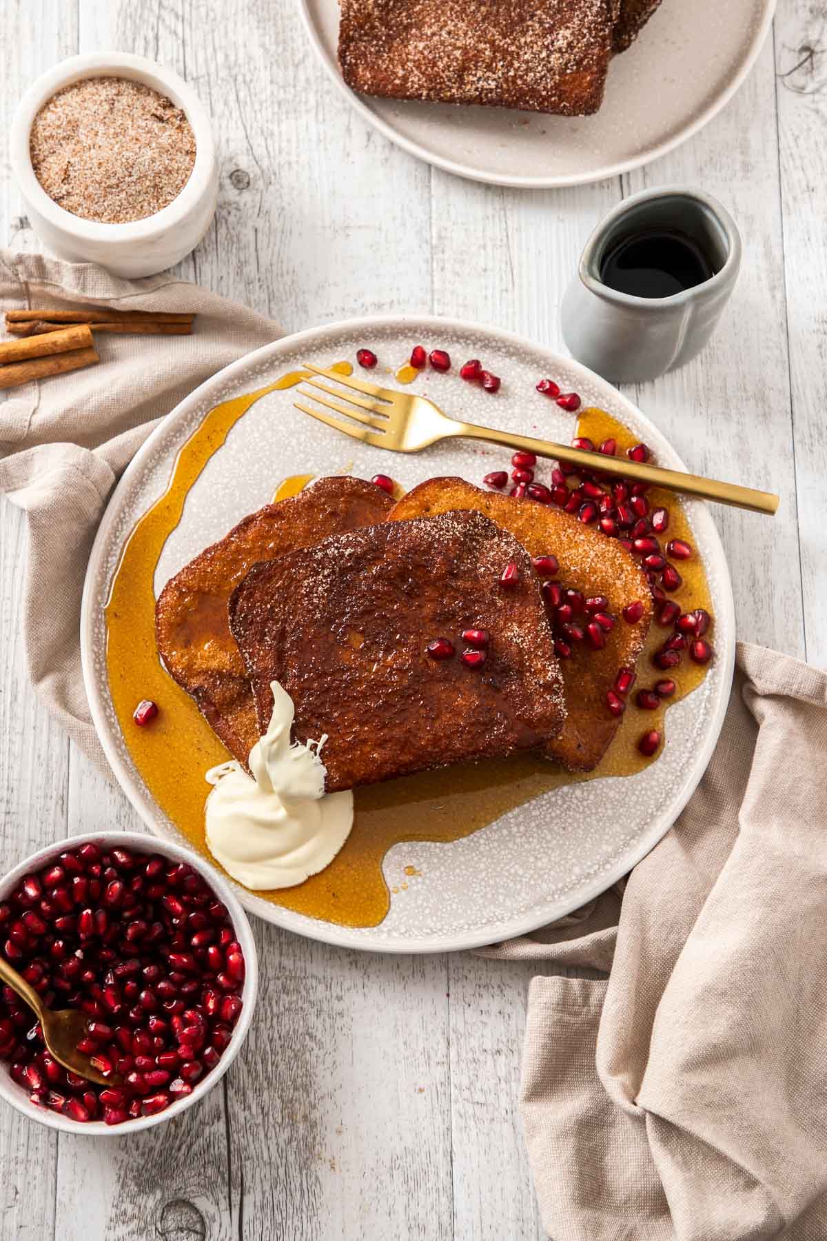 A plate of Cinnamon Sugar French Toast with pomegranate, cream, and maple syrup.