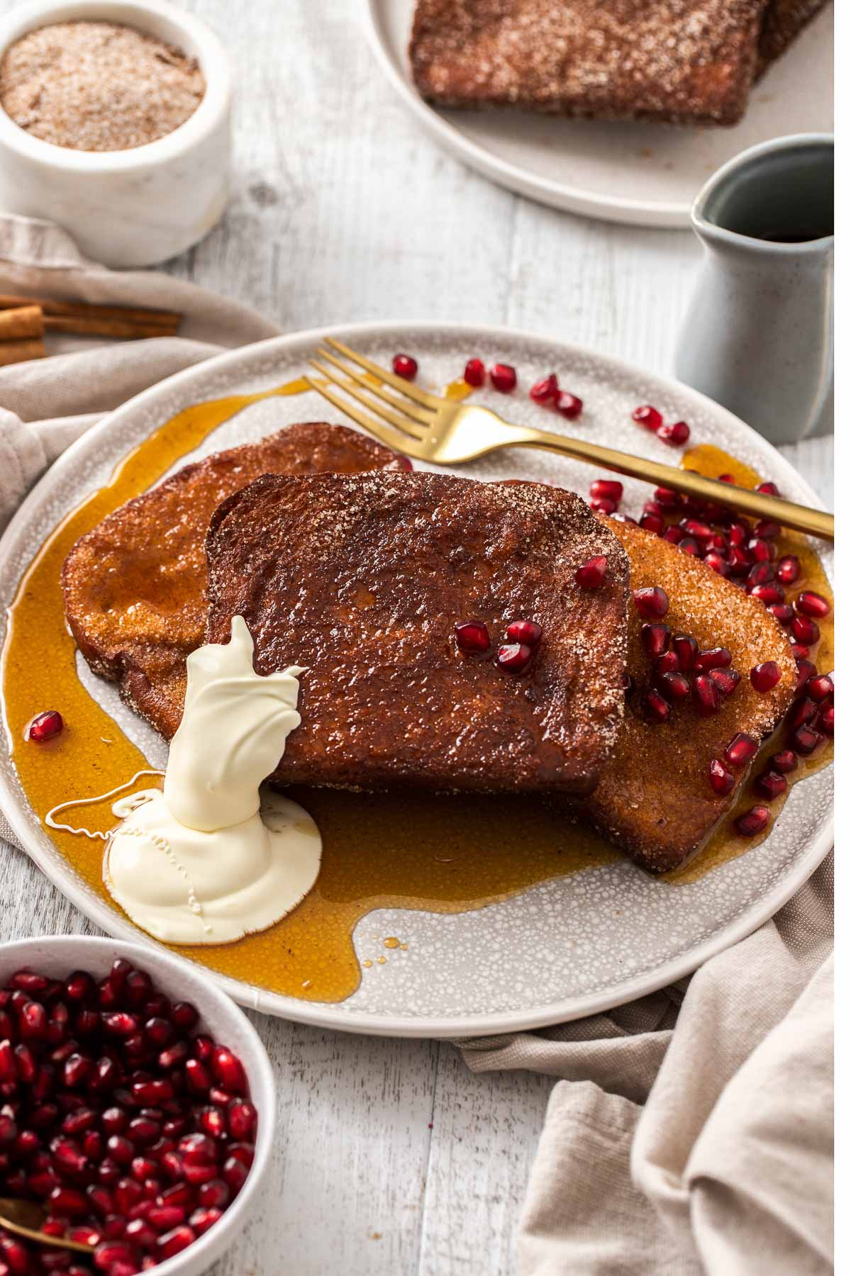A close up of Cinnamon French Toast, garnished with cream, maple syrup, and pomegranates.