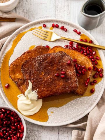 Cinnamon Sugar French Toast on a white plate with cream, maple syrup, and pomegranate.
