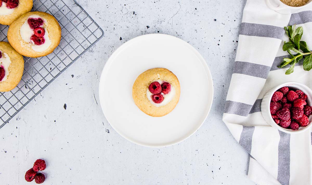 A bright photo of a raspberry cheesecake cookie on a white plate.