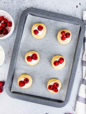 Raspberry cheesecake cookies on a grey baking tray.