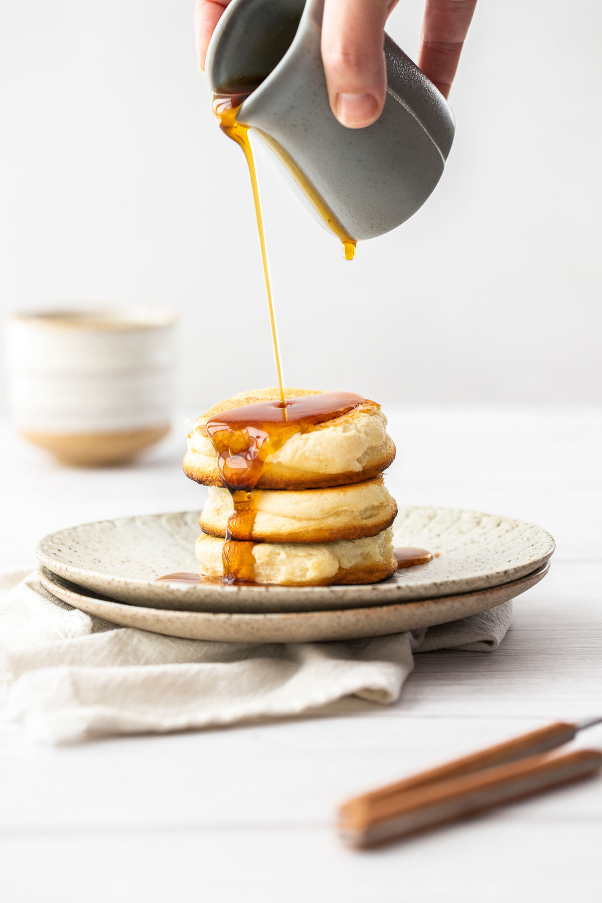 Maple syrup being poured on to a stack of three Japanese souffle pancakes.