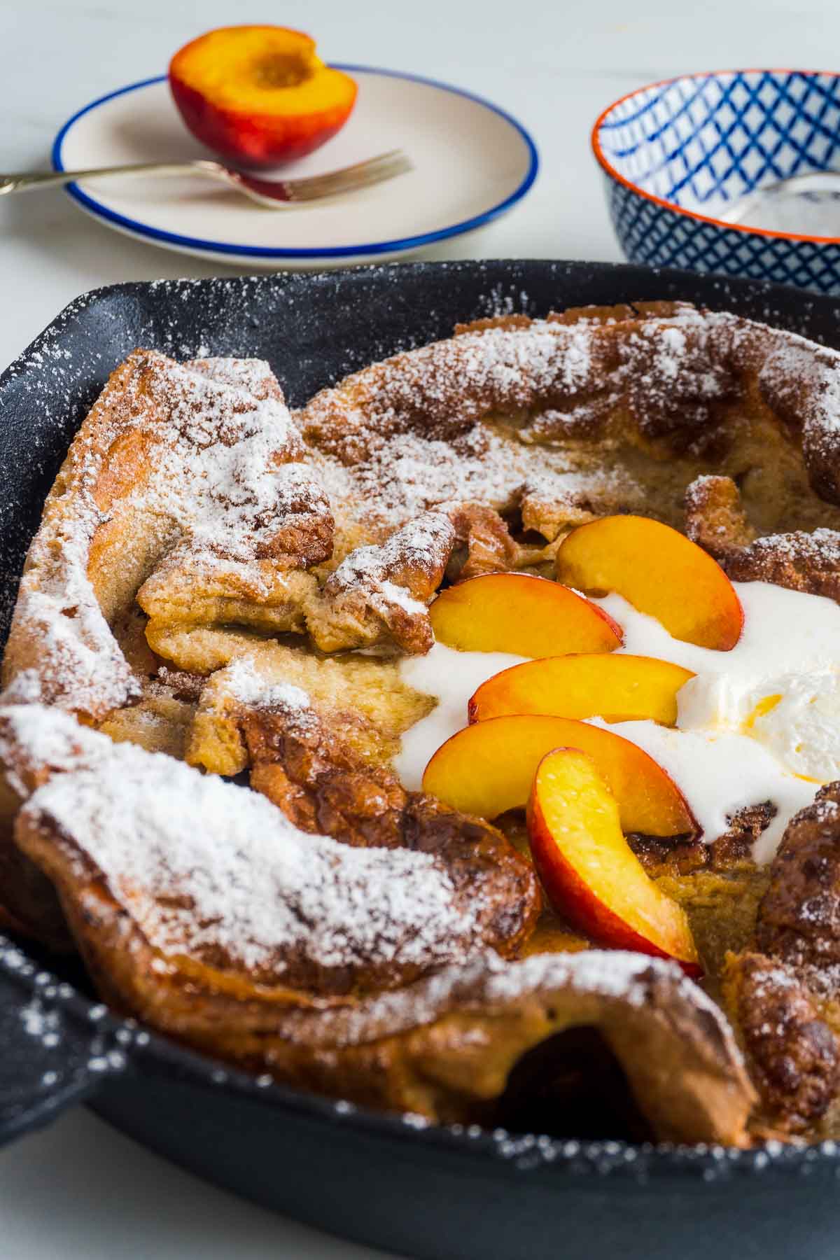 Icing sugar on a Dutch Baby Pancake with Peaches and melted ice cream.