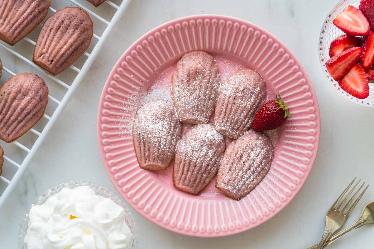 Strawberry madeleines on a plate with fresh strawberries next to them.