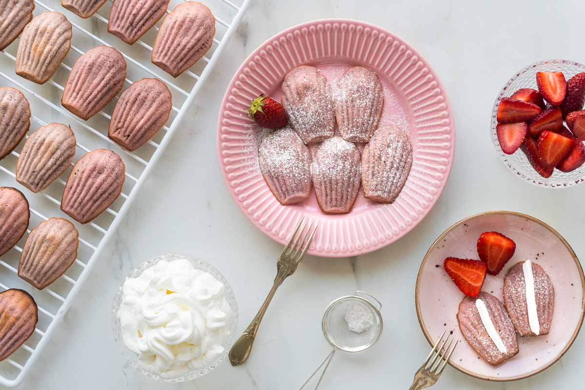 A plate of strawberry madeleines. A second plate it next to it with madeleines and cream.