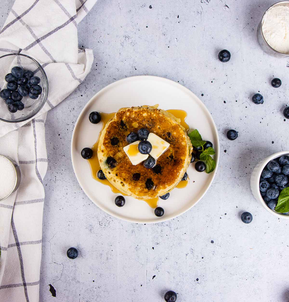 Blueberry pancakes with maple syrup stacked on a white plate.
