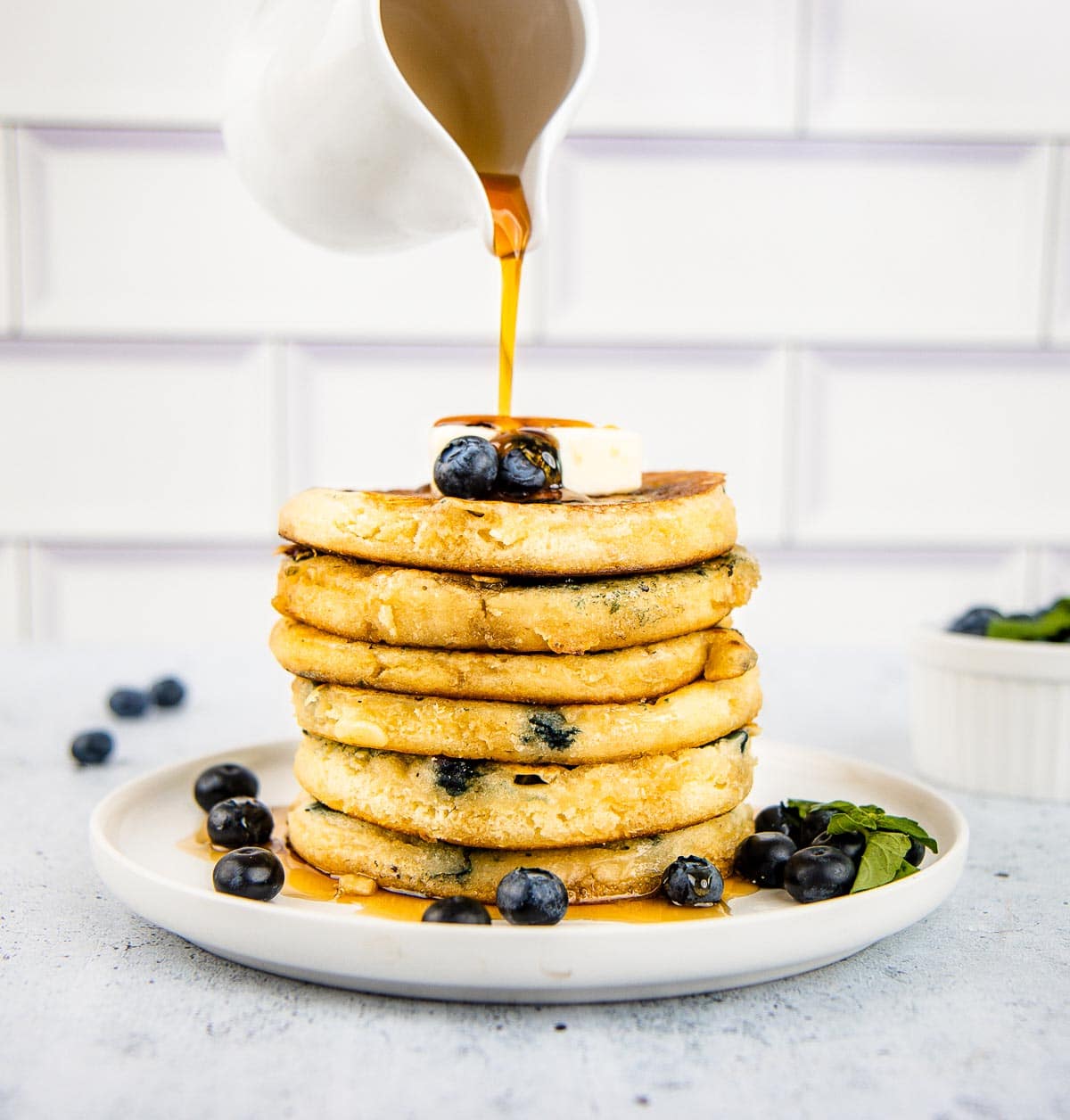 Maple syrup being poured on to a stack of blueberry buttermilk pancakes.