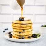 Maple syrup being poured over blueberry buttermilk pancakes.