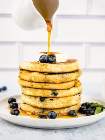 Maple syrup being poured over blueberry buttermilk pancakes.
