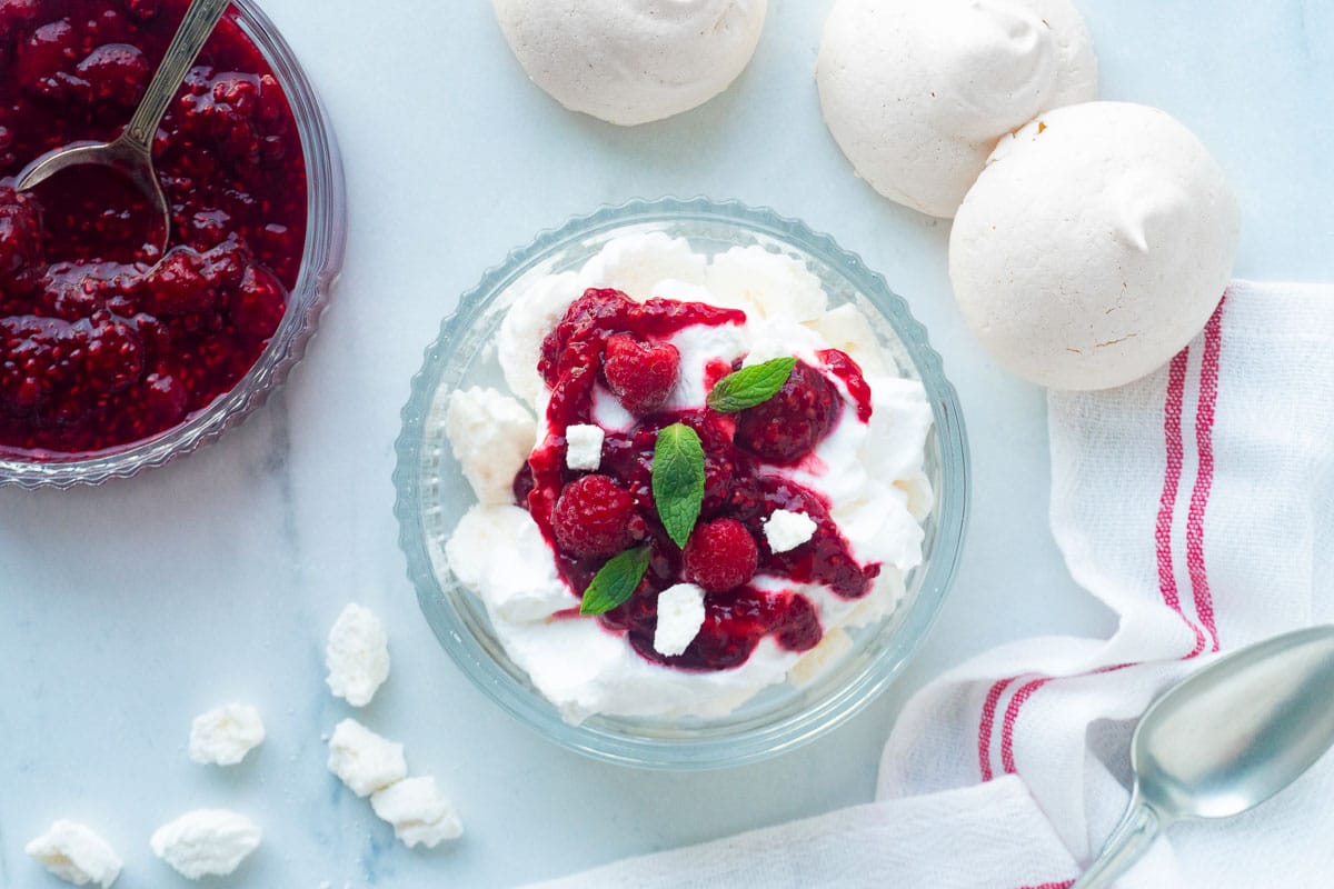 A top down view of a Raspberry Eton Mess with raspberry sauce and meringues on the side.