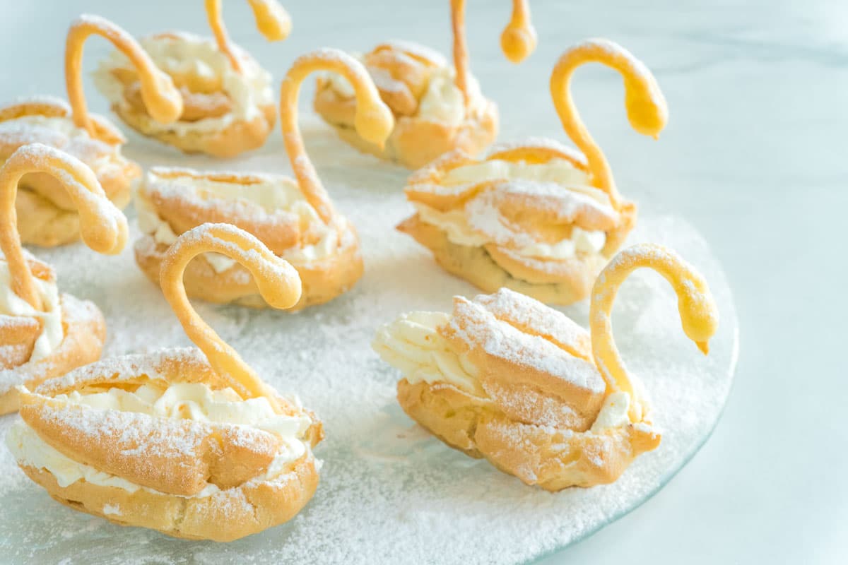 A plate of choux pastry swans that have been dusted with confectioner's sugar.