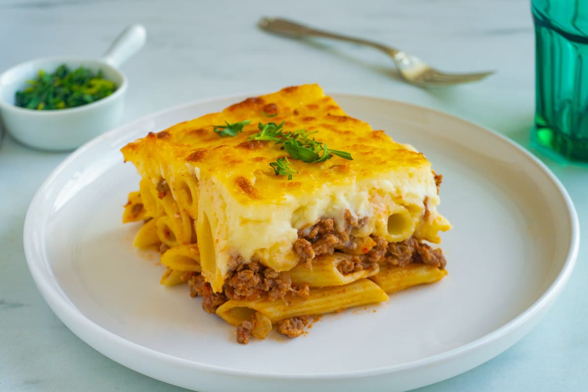 A square slice of macarona bechamel that clearly shows the layers of pasta, meat sauce, and bechamel.