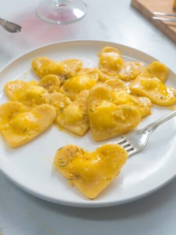 A white plate full of heart-shaped ravioli. A fork points to one ravioli at the front of the plate.