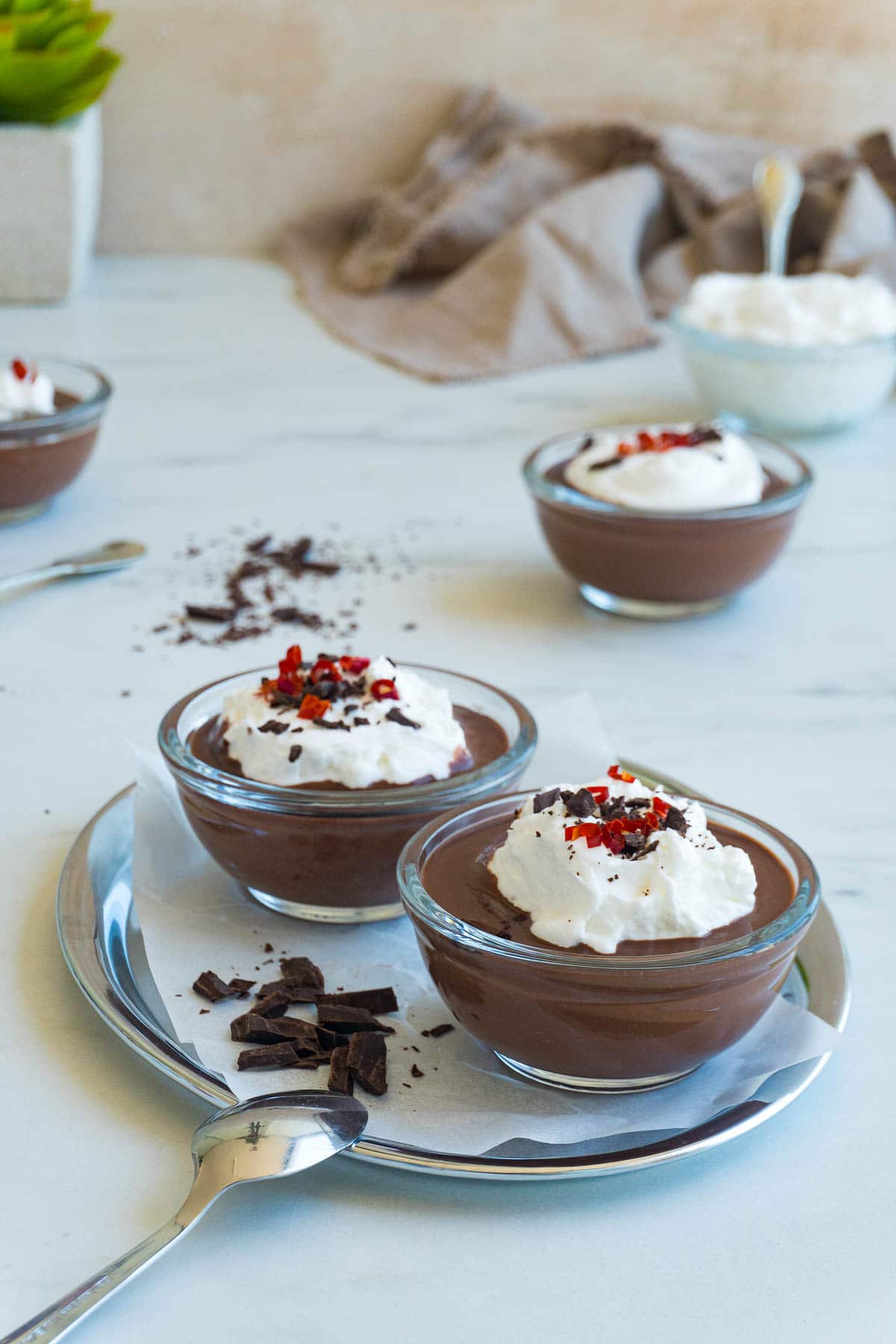 Two dark chocolate puddings on a tray with small chocolate pieces next to them.
