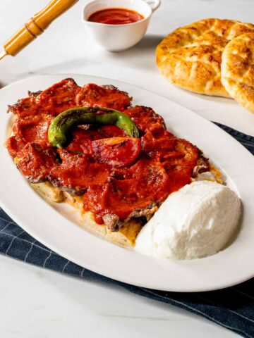 A plate of Iskender Kebab next to some Turkish bread.