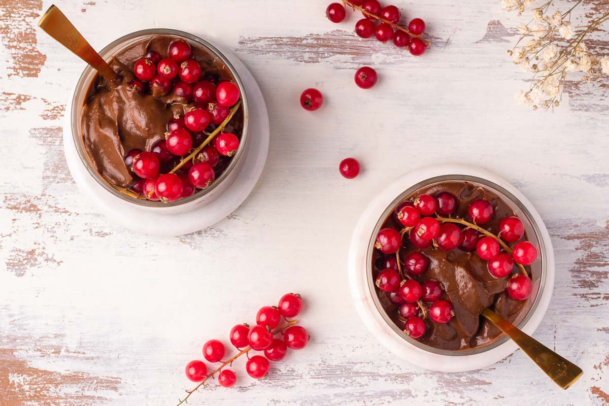 A bird's eye view of two servings of vegan chocolate avocado mousse, decorated with bright red berries.