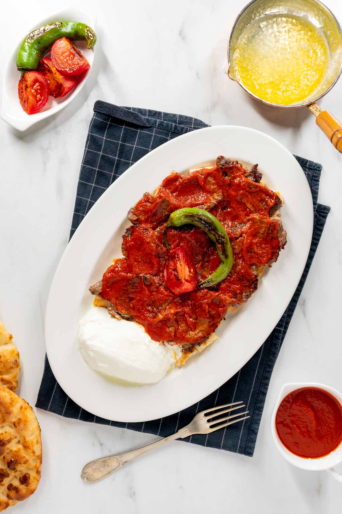 Iskender Kebab on a white plate with a blue napkin underneath it.