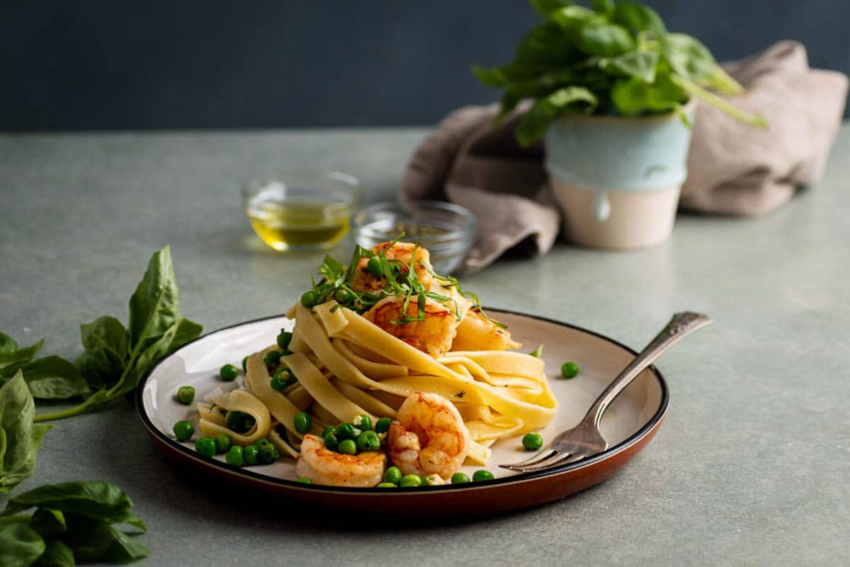 Lemon fettuccine pasta with garlic shrimp and peas on a plate.