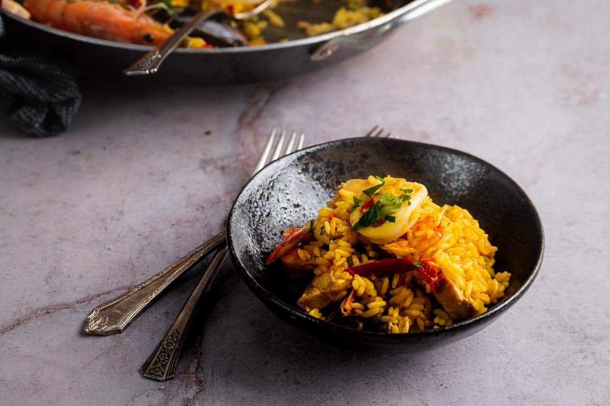 A black bowl filled with yellow paella rice.