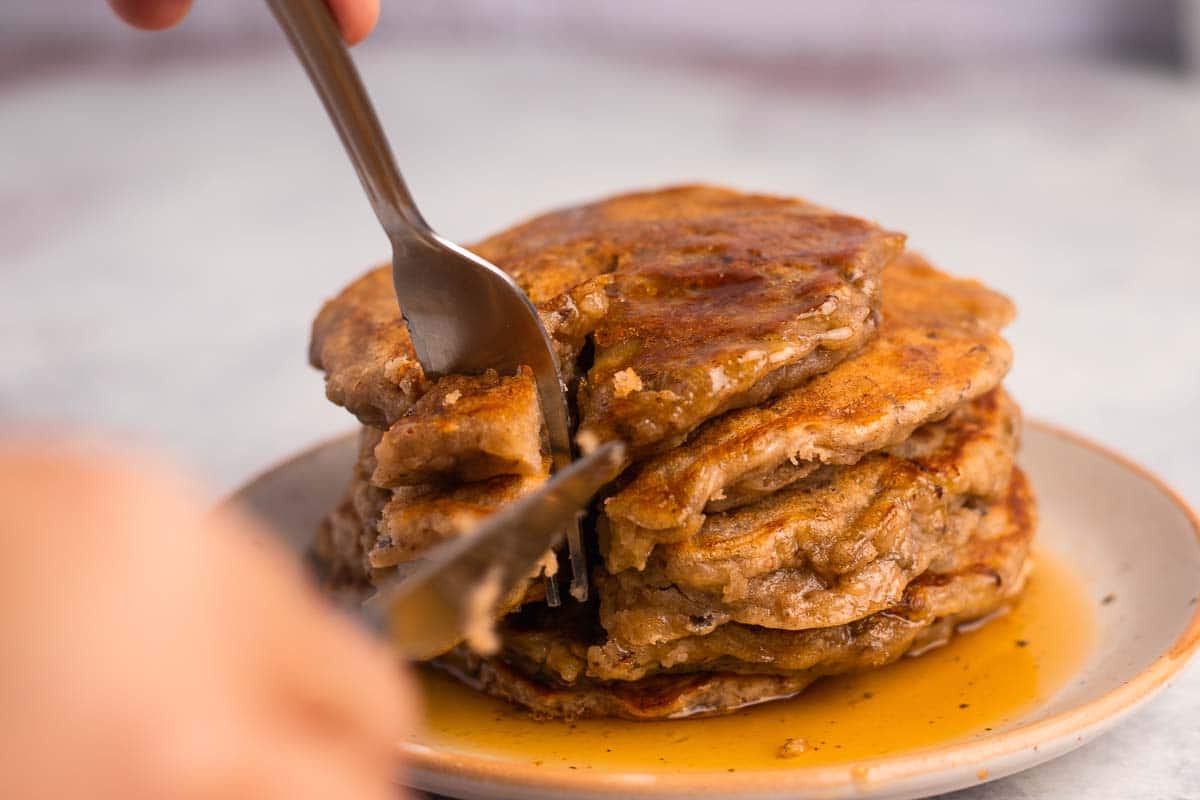 A knife and fork cut into a moist stack of vegan banana pancakes.