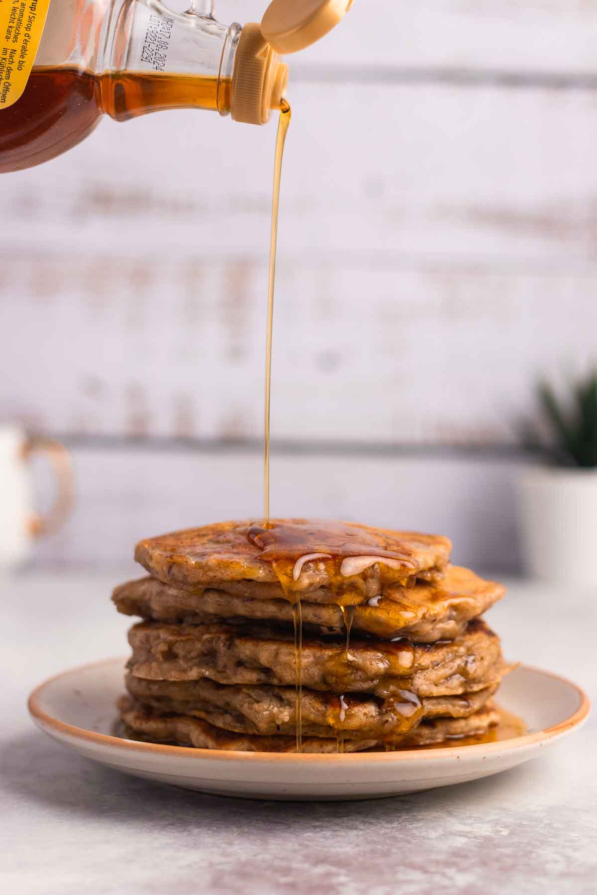 Maple syrup is poured over a stack of vegan banana pancakes.