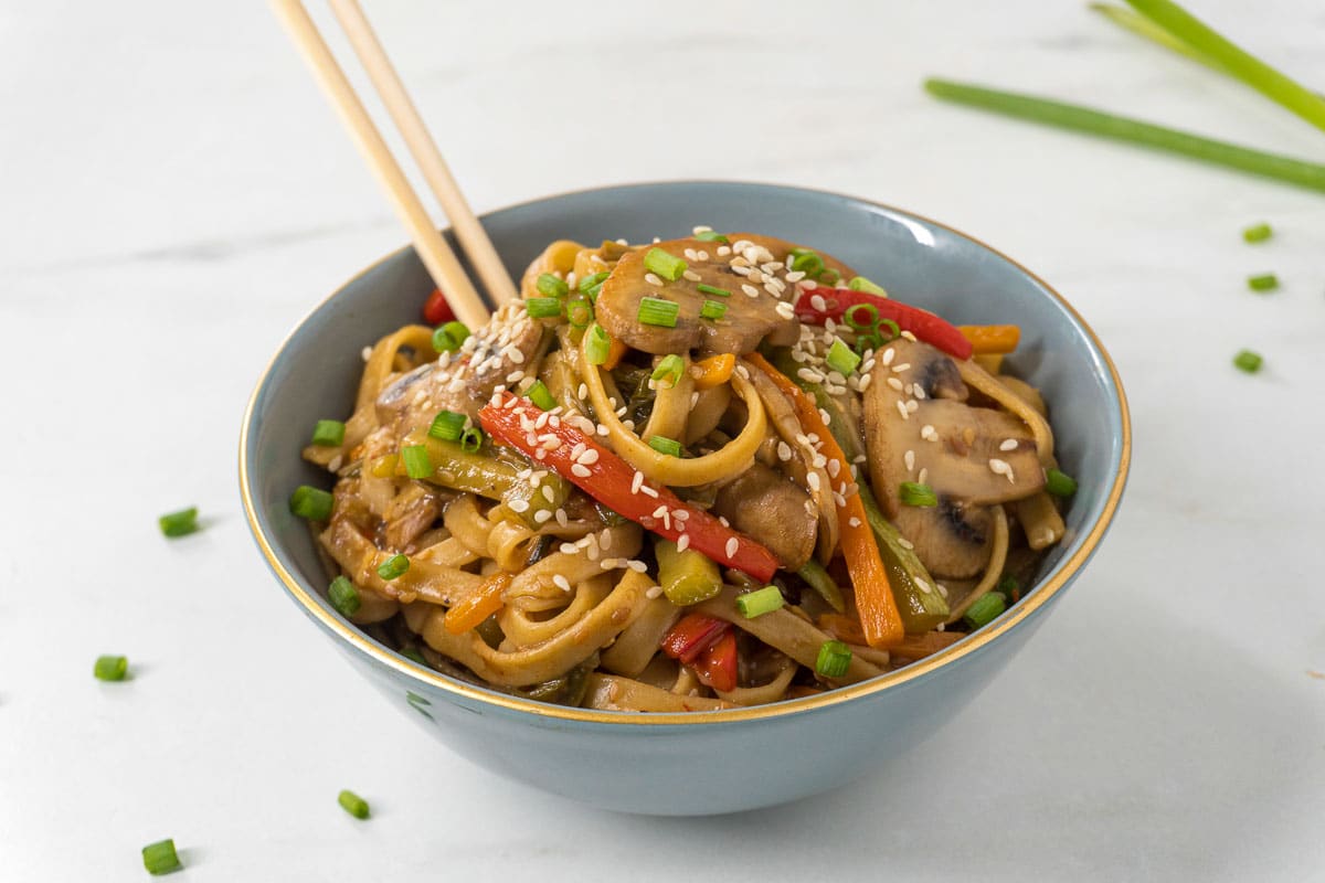 Asian veggie pasta containing mushrooms, peppers, spring onions, and sesame seeds in a bowl.