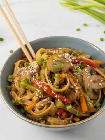 Asian Vegetable Pasta in a blue bowl with a pair of chopsticks dug into the noodles.