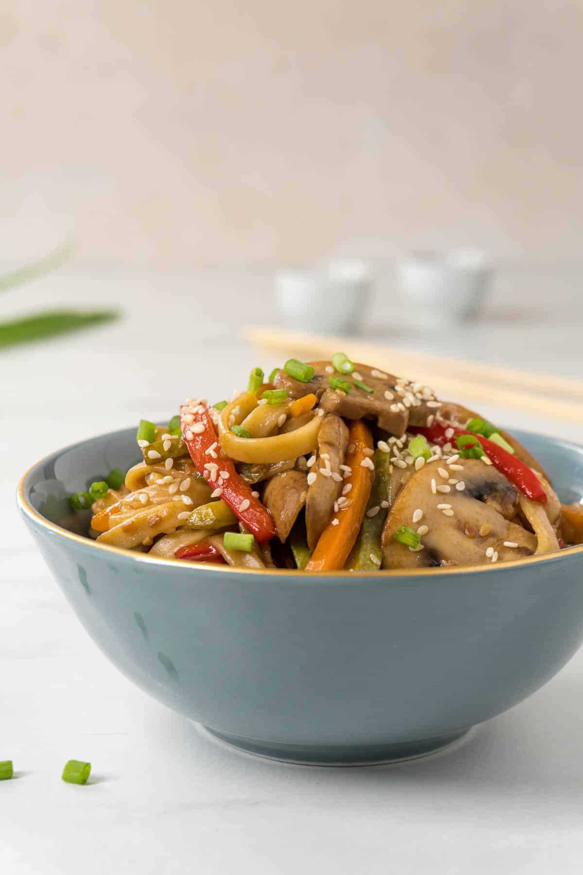 Asian vegetable pasta in a blue bowl. Carrots, red pepper, mushrooms and sesame seeds are clearly visible in the pasta.