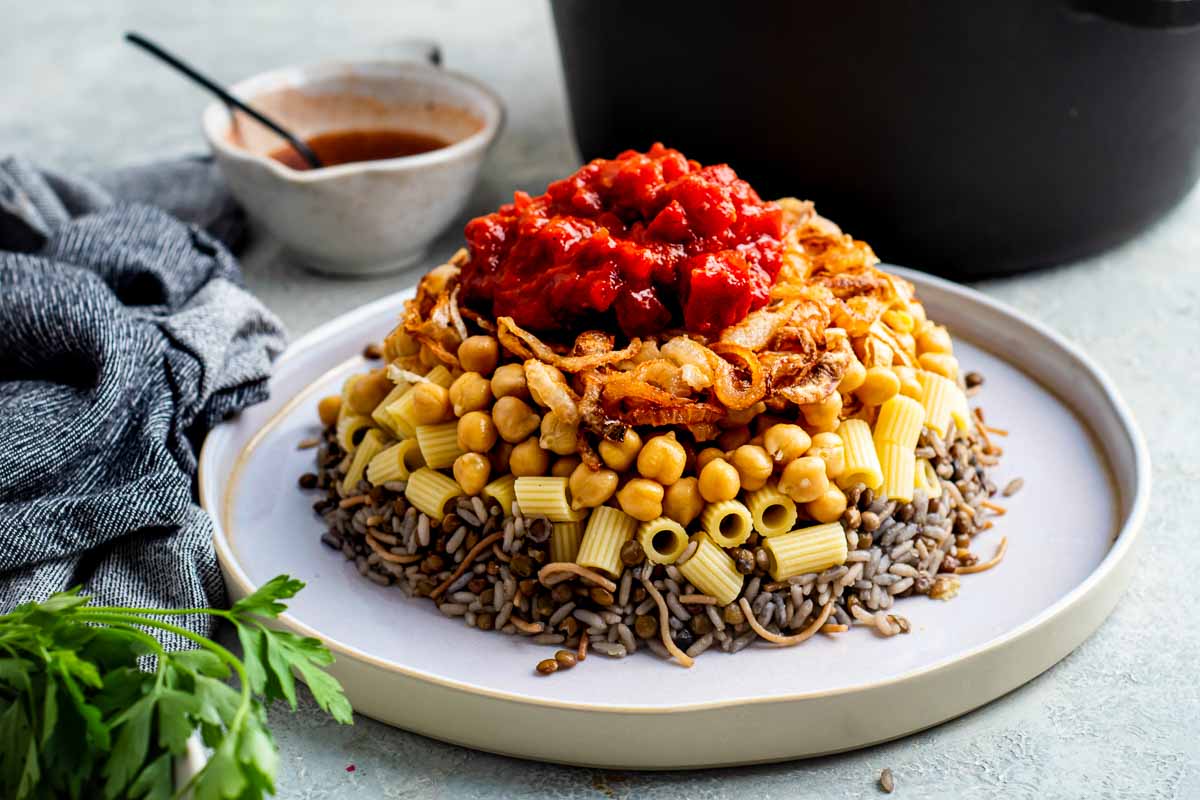 Authentic Egyptian Koshari stacked high on a white rimmed dish.