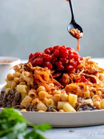 Dukka is drizzled on to Egyptian koshari that is piled high on a white dish.