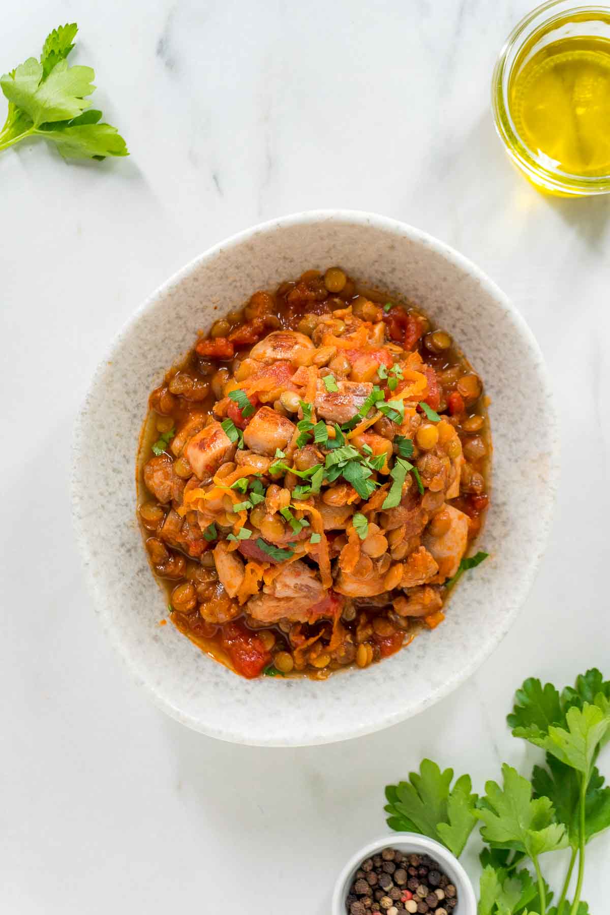 A white bowl full of harissa chicken with lentils. It is garnished with parsely.