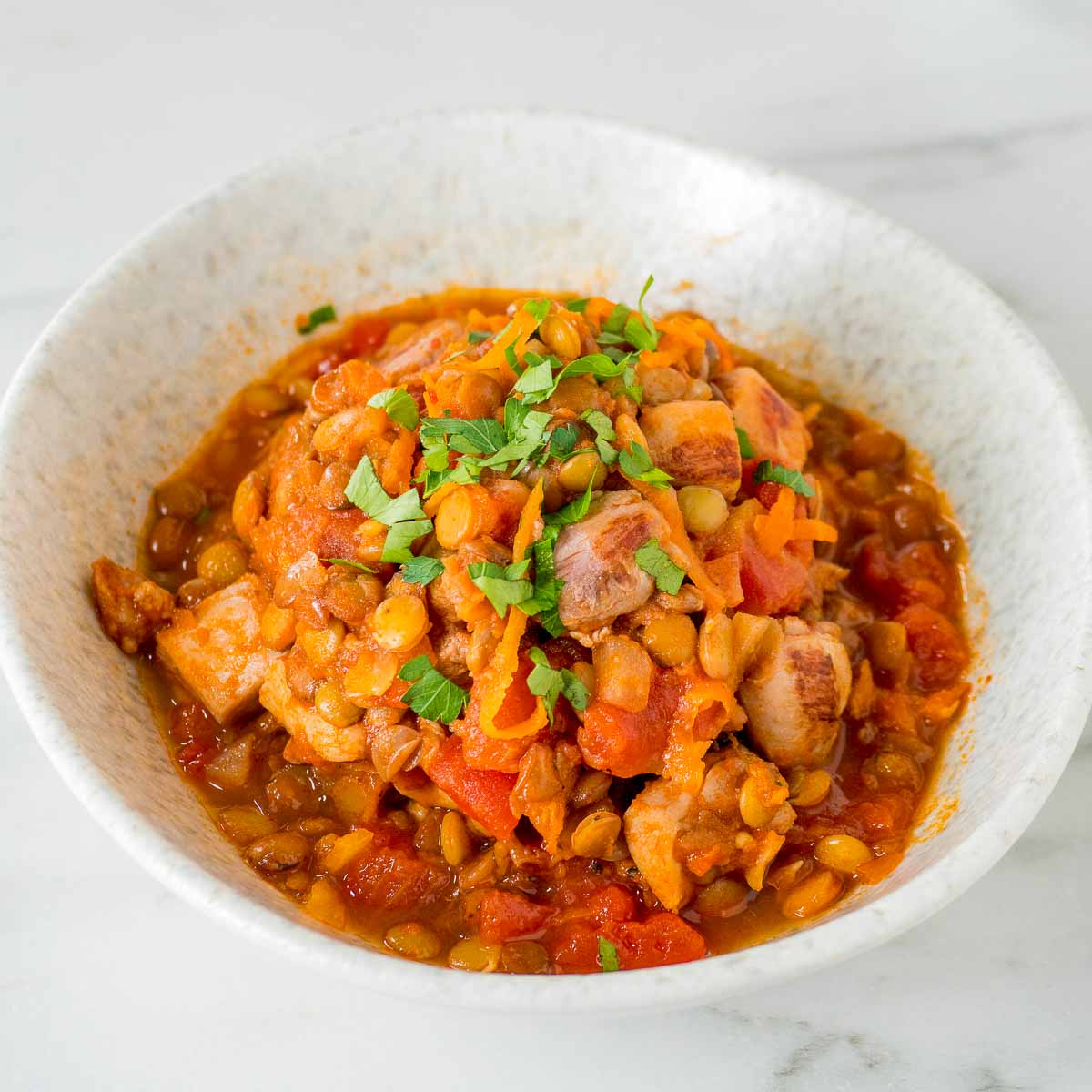 A white bowl filled with chicken cooked with harissa and lentils. 