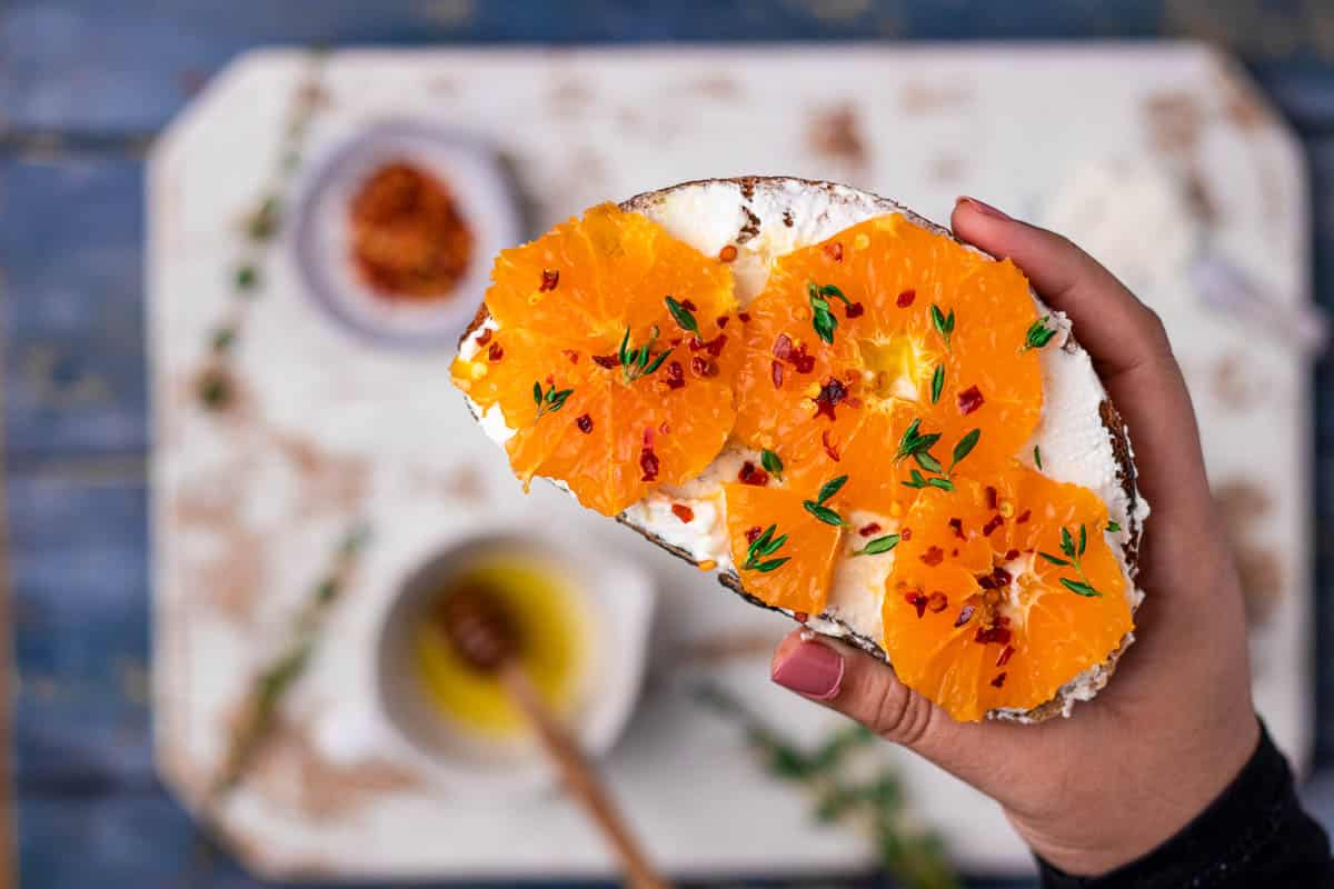 A slice of orange honey ricotta toast being held up to the camera.