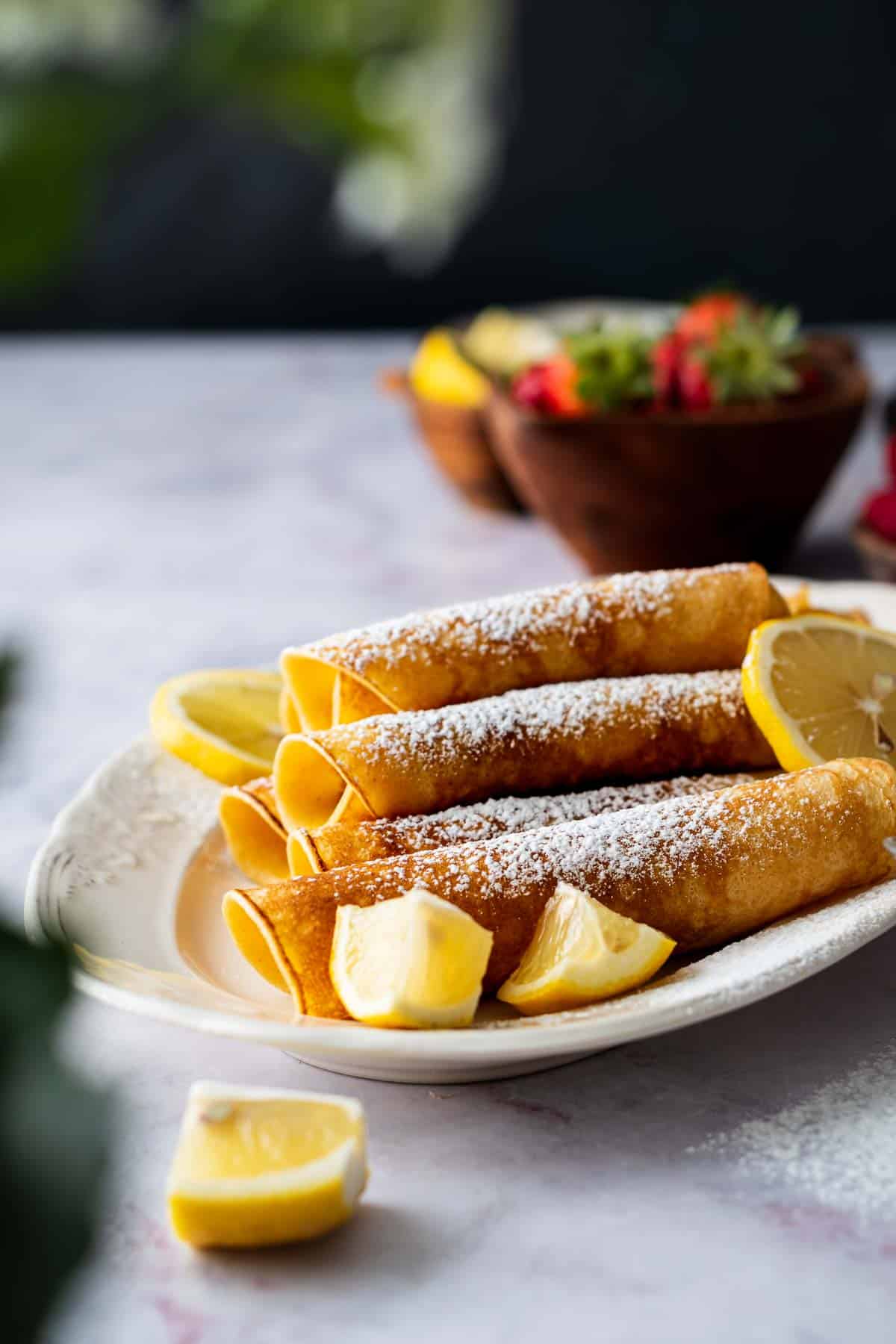 A plate of rolled pancakes served with sugar and lemons.