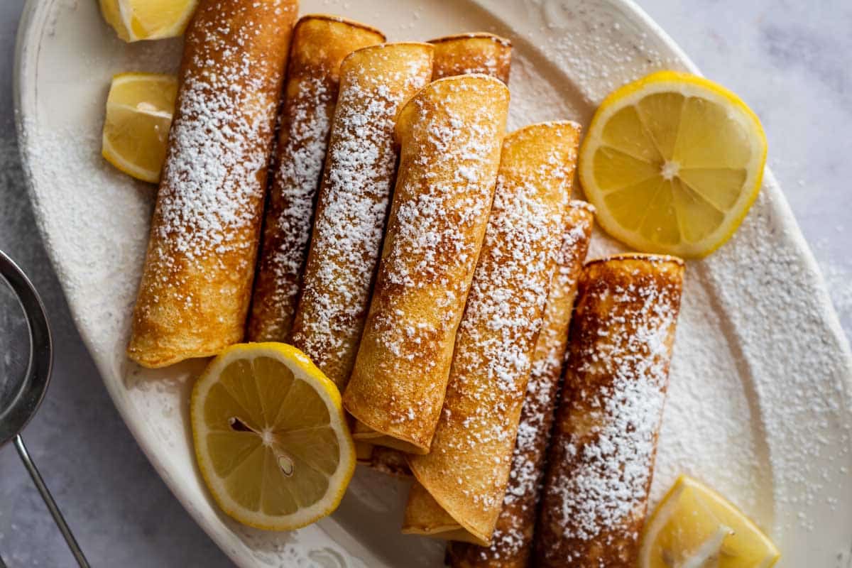 Royal pancakes, rolled and on a white plate served with lemon wedges.