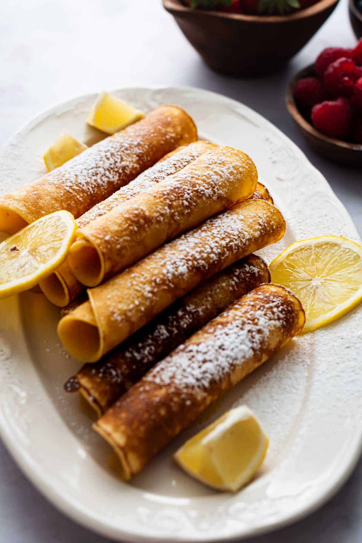Pancakes made using the royal pancake recipe served on a white dish, decorated with lemon wedges and icing sugar.