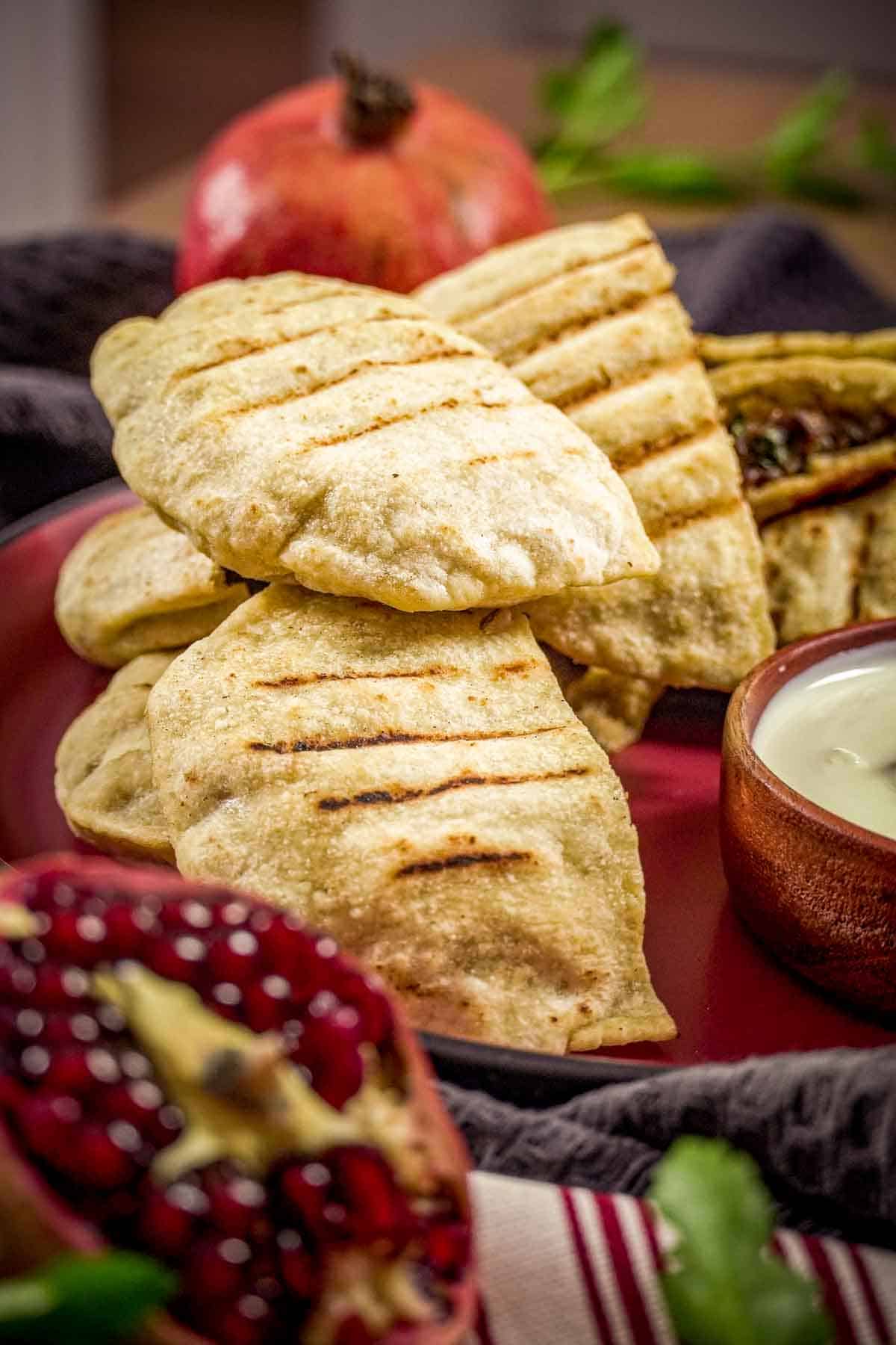 Several stuffed pita rounds on a plate, decorated with toum and pomegranate.
